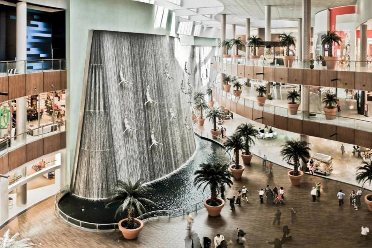 Interior of a large, modern shopping mall with a fountain.